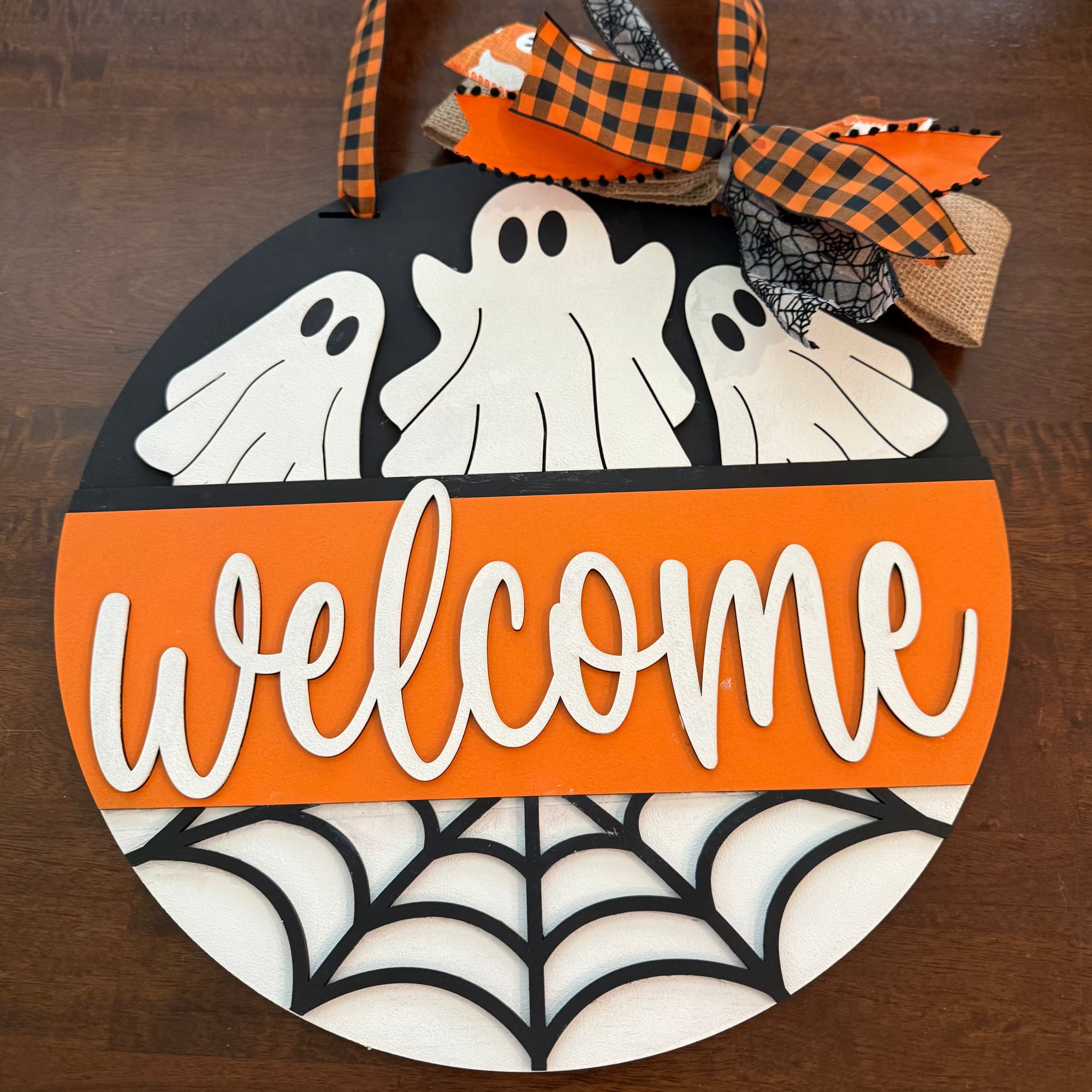 Halloween-themed door sign with ghosts, spider web, and 'welcome' text on an orange and black background.