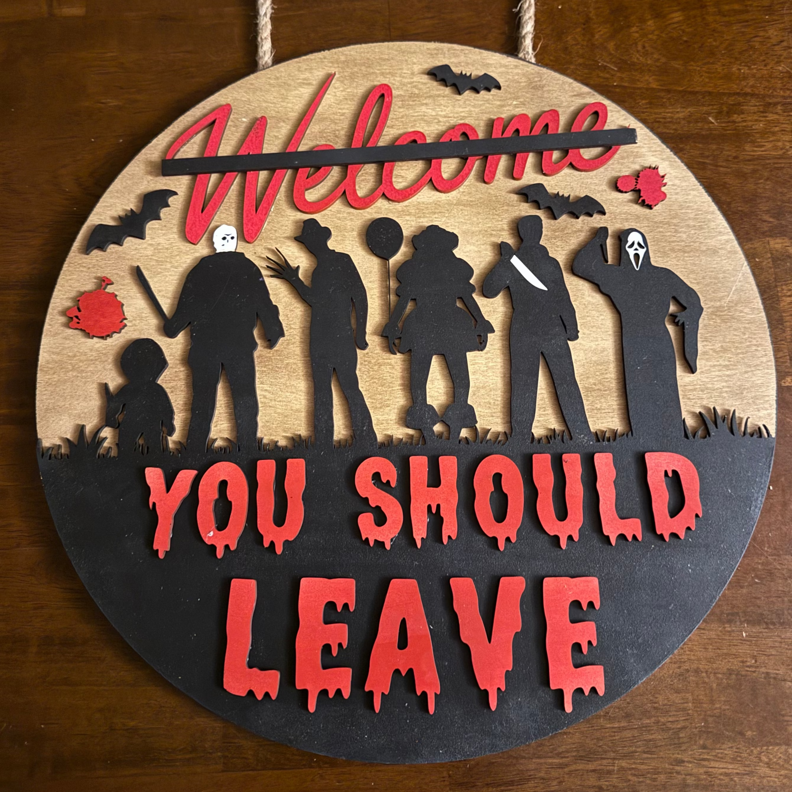 Decorative sign with silhouettes and text on a wooden board, hanging against a wooden background.